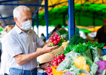 retired european man wearing medical mask protecting against the virus buying radishes and cabbage in market