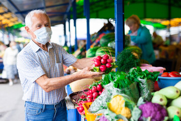 retired european man wearing medical mask protecting against the virus buying radishes and cabbage...