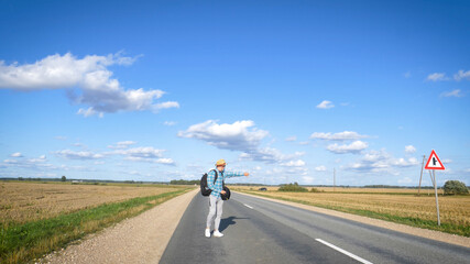 A young man is hitchhiking around the country. The man is trying to catch a passing car for traveling. The man with the backpack went hitchhiking to south.