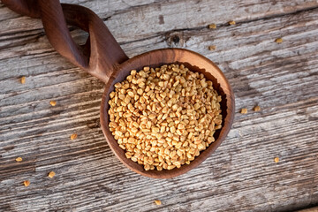 Fenugreek seeds on a wooden spoon on a table