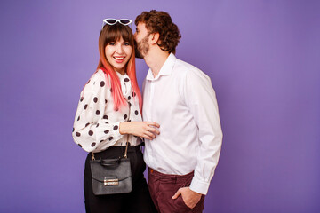 Elegant  couple in love hugging and looking on camera. Handsome  man with beard and his pretty woman with pink hairs in stylish retro outfit posing on purple background in studio.
