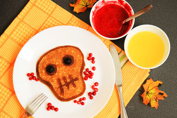 Halloween breakfast. pancake in the form of a skull with eyes of olives served with honey and cranberry jam