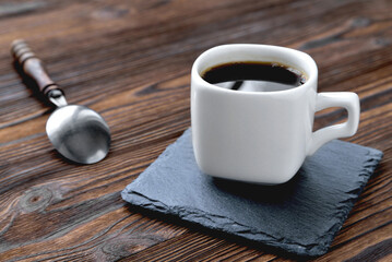 white cup with coffee on a stone stand, vintage coffee spoon, wooden natural background close up