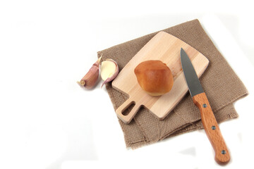 bun on a cutting board on canvas napkin, cloves of garlic and a kitchen knife on white background flat lay