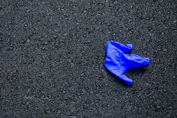 A Used Blue Medical Glove On a Blacktop Road To Protect From COVID-19