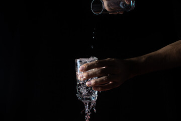 Water on a black background. A glass overflowing with water. Water is poured out of the glass. Pure...