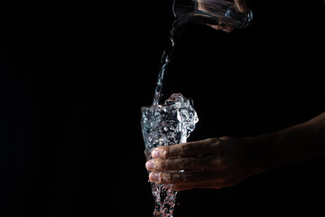 Water on a black background. A glass overflowing with water. Water is poured out of the glass. Pure water