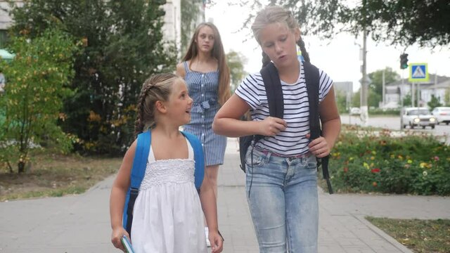 group of schoolchildren walking to school along the path. happy family school concept.little schoolgirl with backpack and textbook. schoolgirls walk along in the park to school for lessons education