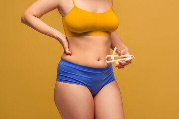 Beauty woman in colorful underwear measuring her body fat with caliper on yellow background