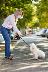 Mature woman walking with a dog outdoors an antivirus mask