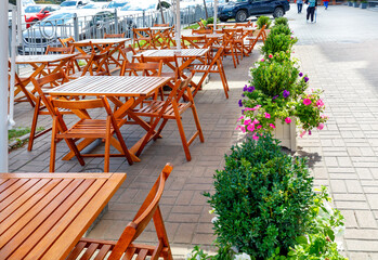 A deserted city street cafe, empty tables and chairs on the sidewalk under a canopy.