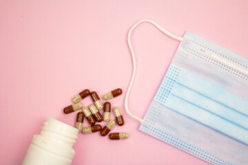 capsules and medical mask on a pink background