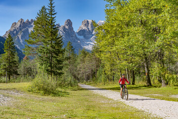 Fototapeta premium nice and active senior woman riding her electric mountain bike on an old railway embankment in the Hoehlenstein valley between Toblach and Cortina Dampezzo, Three Peaks Dolomites, South Tirol, Italy