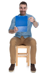 Positive smart casual man holding clipboard, smiling and pointing forward