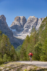 Fototapeta na wymiar nice and active senior woman riding her electric mountain bike on an old railway embankment in the Hoehlenstein valley between Toblach and Cortina Dampezzo, Three Peaks Dolomites, South Tirol, Italy