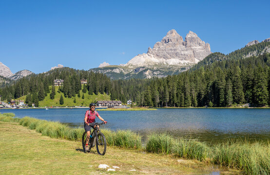 nice senior woman ridung her electric mountain bike at the shore of Misurina Lake below the famous summits of the Three peak of Lavaredo in the Dolomites mountains in South Tirol, Italy © Uwe
