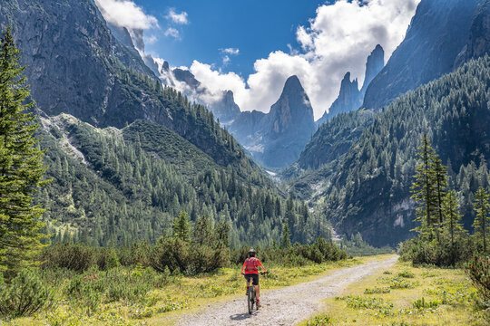 pretty senior woman riding her electric mountainbike in the Fischlein Valley in the Sexten Dolomites wit famous Sextan sundial in background, Tre cime National park, South Tirol, Italy 
