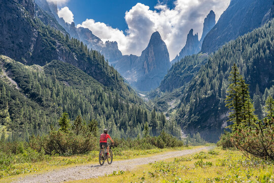 pretty senior woman riding her electric mountainbike in the Fischlein Valley in the Sexten Dolomites wit famous Sextan sundial in background, Tre cime National park, South Tirol, Italy 