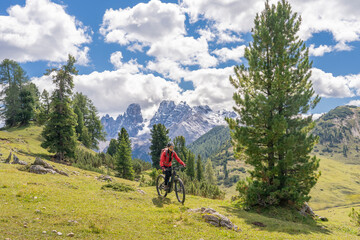 Fototapeta na wymiar nice and active senior woman riding her electric mountain bike on the high plateau of Pratto Piazzo in the three peaks Dolomites , rocky silhouette of Mount Cristallo in background, South Tirol, Italy