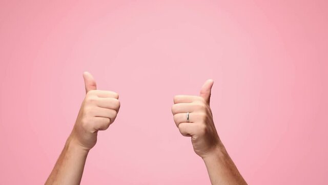 man holding hands above head, making thumbs up gesture, joining and pressing hands on pink background
