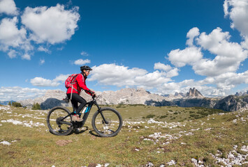 Fototapeta na wymiar nice senior woman, riding her electric mountain bike below the famous Three peak of Lavaredo in the Sexten Dolomites in South tyrol, Italy
