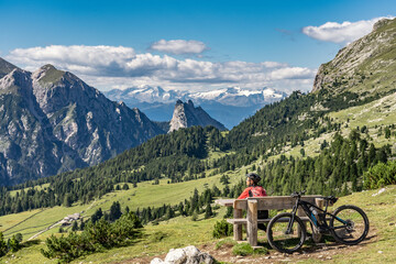 nice and active senior woman riding her electric mountain bike on the high plateau of Pratto Piazzo in the three peaks Dolomites , rocky silhouette of Mount Cristallo in background, South Tirol, Italy - obrazy, fototapety, plakaty