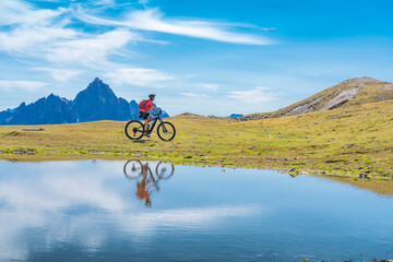 Fototapeta na wymiar nice woman riding her electric mountain bike the Three Peaks Dolomites, reflecting herself in the blue water of a cold mountain lake
