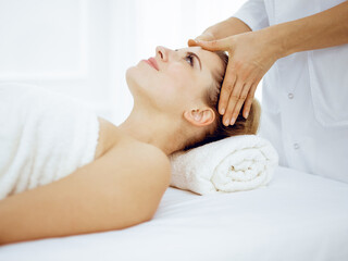 Fototapeta na wymiar Young and blonde woman enjoying facial massage in spa salon. Beauty concept