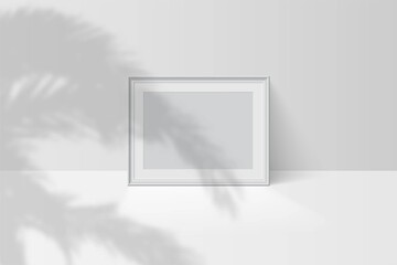 Tropical palm leaf shadow falls on blank horizontal white picture frame
