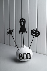 Halloween home decorations. Painted white pumpkin and black Halloween scary shadow puppets on sticks against a white wooden wall. Copy space, vertical orientation. Isometric style.