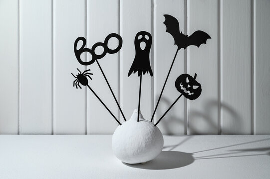 Halloween Home Decorations. Painted White Pumpkin And Black Halloween Scary Shadow Puppets On Sticks Against A White Wooden Wall. Copy Space