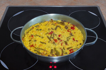 Typical Spanish dish made with rice, vegetables, meat, and seafood on a huge frying pan on top of a modern ceramic hob. Rustic kitchen, cooking healthy food at home.