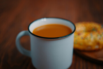 Mug of fragrant cocoa and a sweet doughnut with yellow glaze and sprinkles. White metal mug with a drink and pastries on a wooden table. Autumn breakfast.