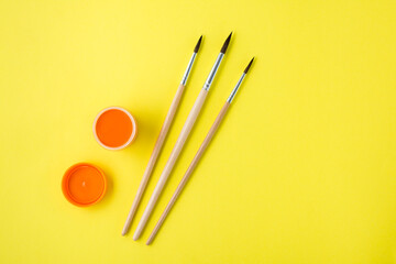 Orange gouache in an open jar and brush on a yellow background. Creative leisure. Copy space