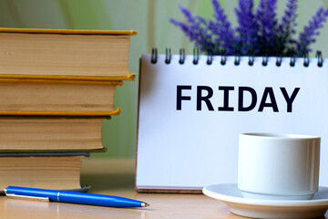FRIDAY - word in a notebook on a background of old books with pen and white cup