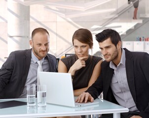 Business team looking at laptop computer screen at office. Confident, busy, successful, thinking, suit, small smile.