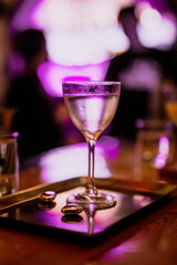 A lifestyle atmospheric photo of a cocktail in a nick and nora glass at the bar in the evening, people in the background, high iso, selective focus