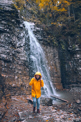 Obraz premium portrait of woman in yellow raincoat in front of autumn waterfall