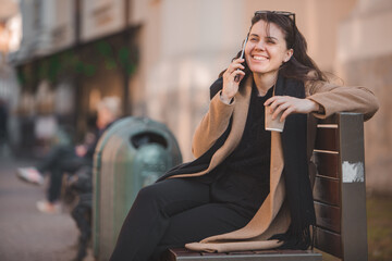 woman sitting on the bench talking on the phone drinking coffee