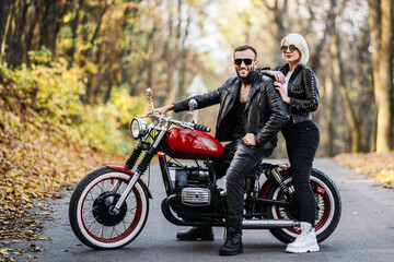 Obraz na płótnie Canvas Pretty couple near red motorcycle on the road in the forest with colorful blured background