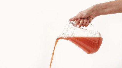 Hand pouring juice, fruit compote from jug isolated over white background