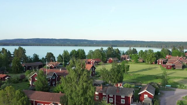 Red wooden houses in drone shot. Aerial view of village and lake in Sweden