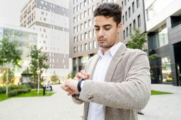 Young serious businessman in formalwear looking at smartwatch on wrist