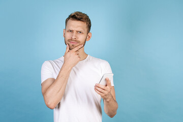 Thoughtful young adult man holding modern smartphone
