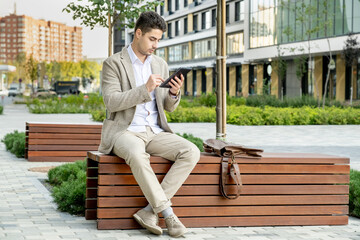 Fototapeta premium Young elegant restful businessman in formalwear sitting on wooden bench in park
