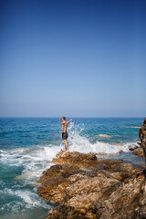 A young man stands on the rocks overlooking the open Mediterranean Sea. A guy on a warm summer sunny day looks at the sea breeze