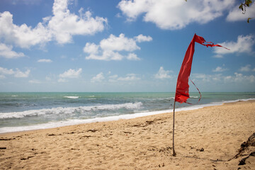 warning sign of a red flag at a beautiful empty tropical beach with a blue sky and  sea