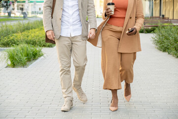 Low section of two young business partners or colleagues moving along large park