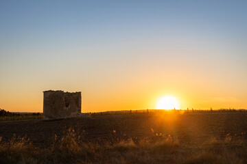 Obraz premium Abandoned old tower in the Spanish countryside at sunset time. Sun hiding behind a wheat field after harvesting season. Summer time, dry hot weather. Editing space. Sebúlcor, Soria, near Madrid, Spain
