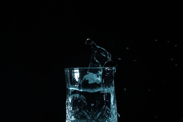 splash of water in a glass by ice cube on black background